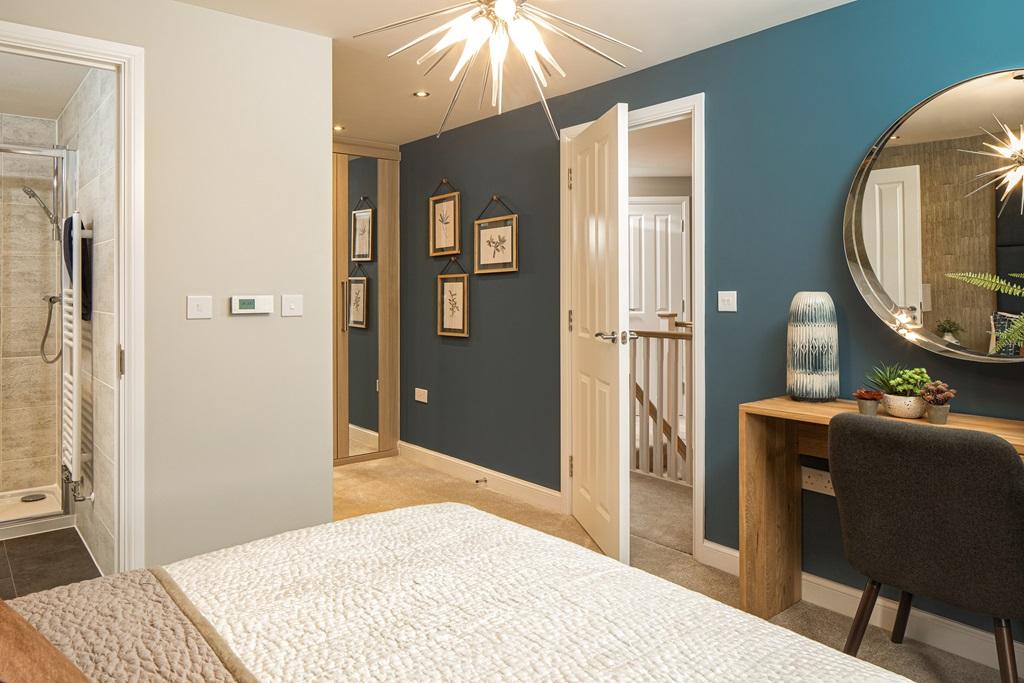 Bedroom with a deep blue wall. There's a desk with a chair and the open door shows an en suite showe
