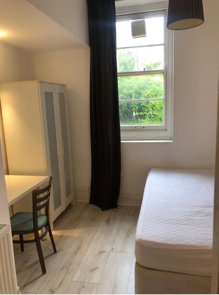 A tidy and well-lit single bedroom with a desk ...