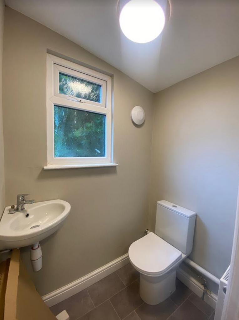 A clean and well lit single toilet with a sink ...