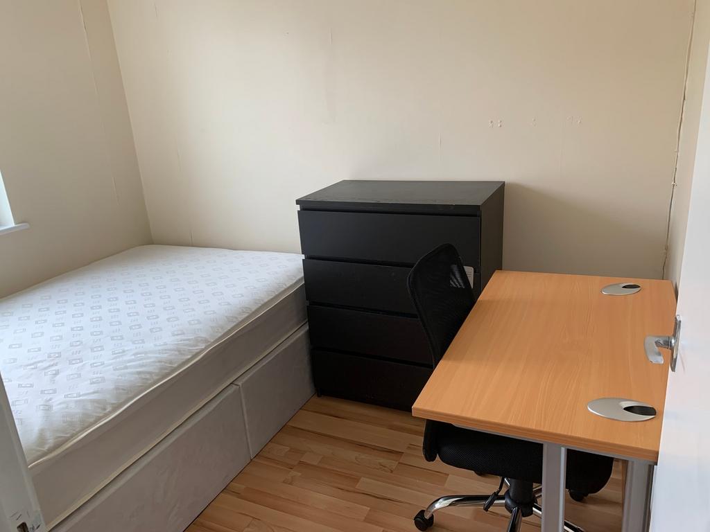 A tidy single bedroom with a comfortable desk a...
