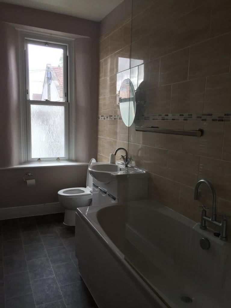 A clean and well lit bathroom featuring a bath ...