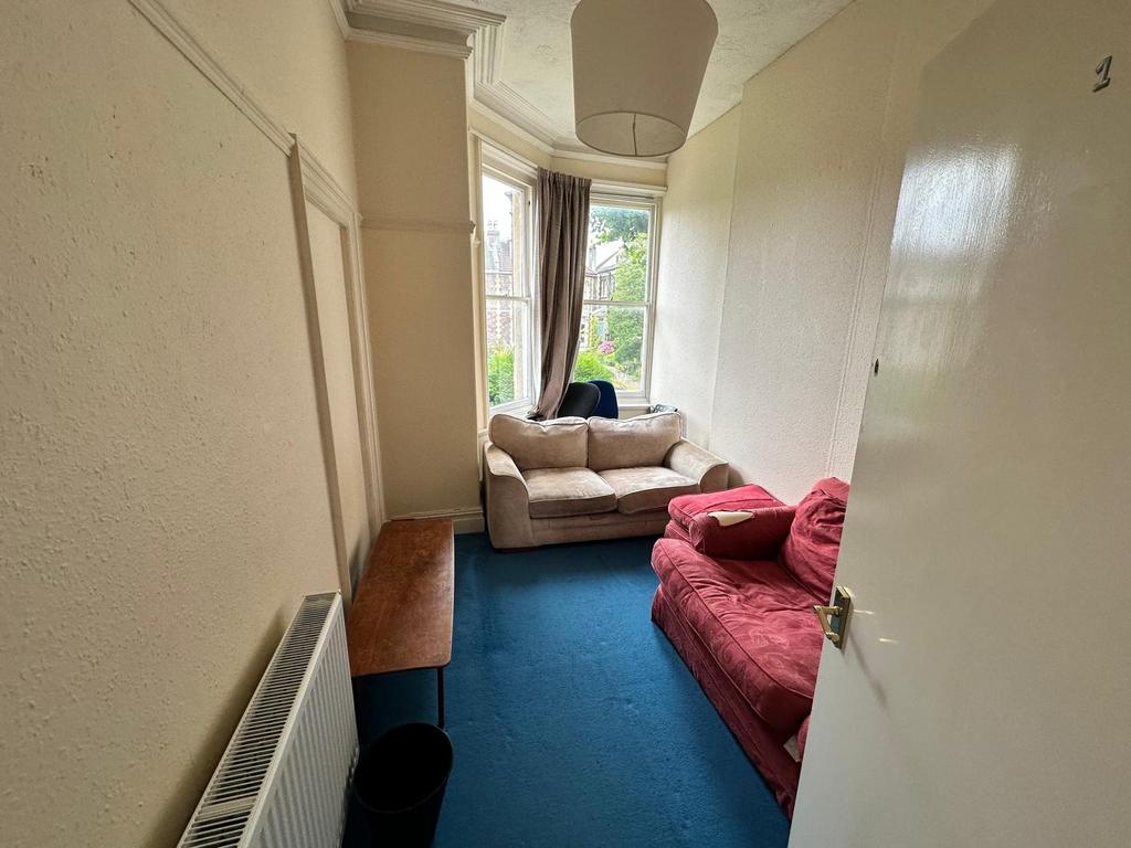 Bright communal lounge with a bay window, two c...