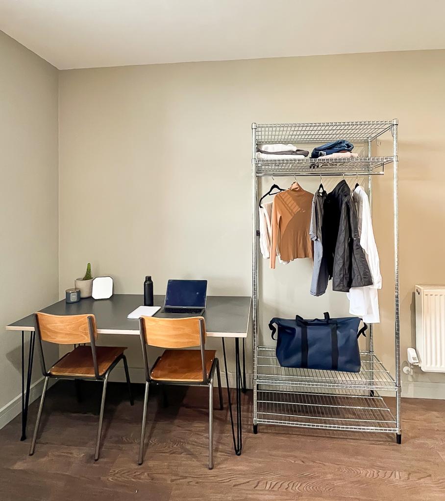 A tidy study area with a desk and clothes rack,...