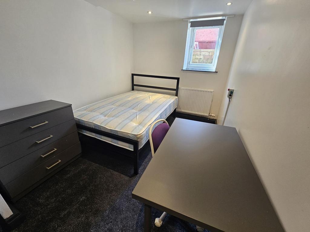 A neat and simple bedroom featuring a bed, a de...