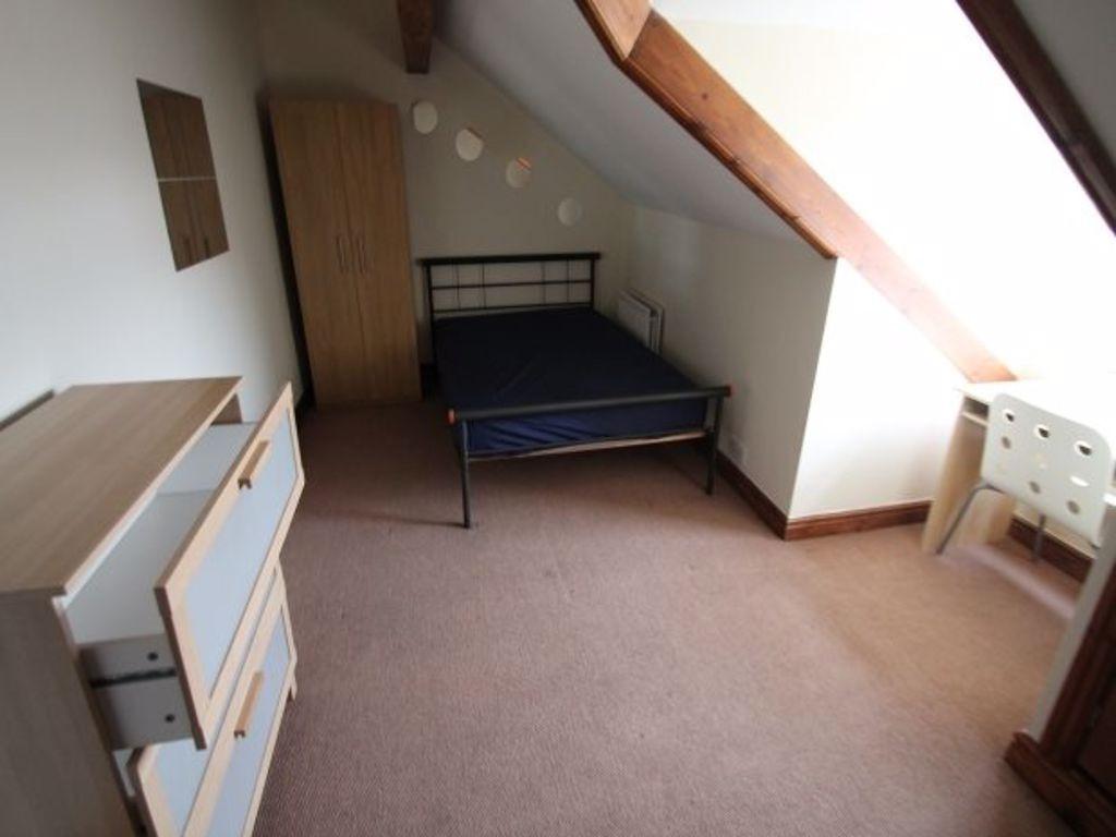 A cozy single bedroom featuring a slanted ceili...