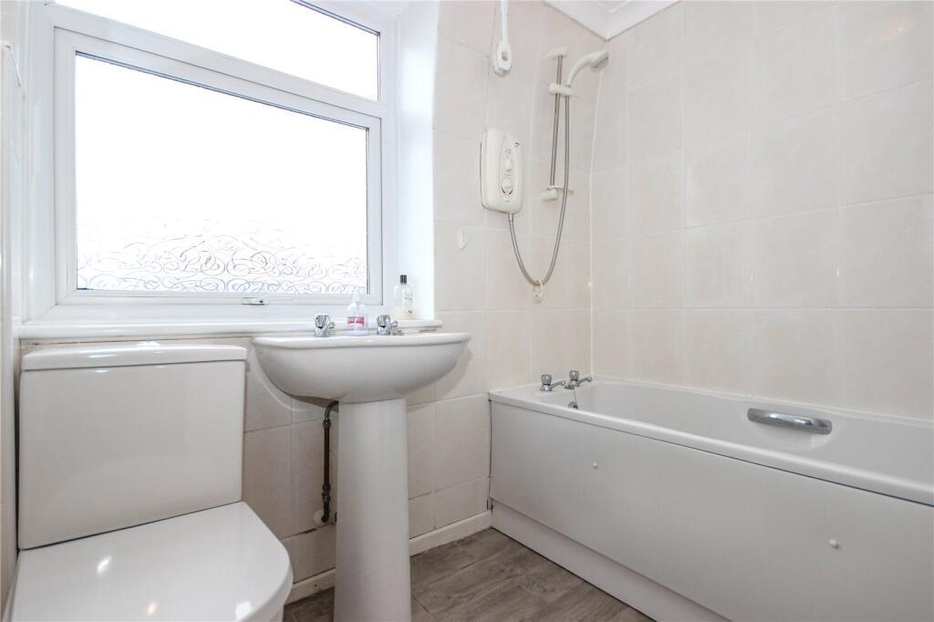 A clean, well-lit bathroom featuring a bathtub,...