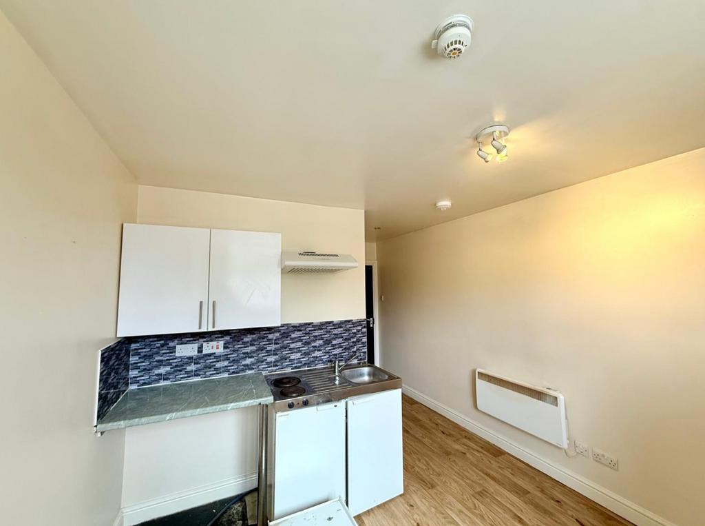 Compact kitchen area featuring white cabinetry,...