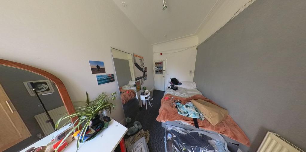 A cozy single bedroom featuring a bright worksp...