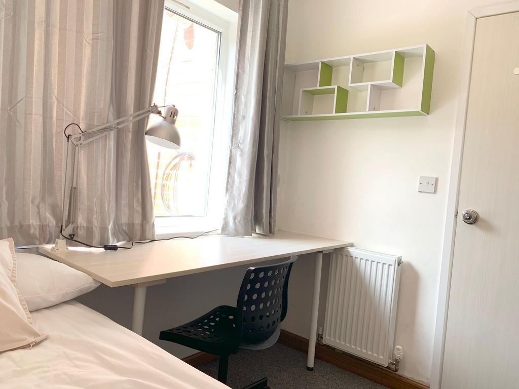 A cozy single bedroom with a neat study desk po...