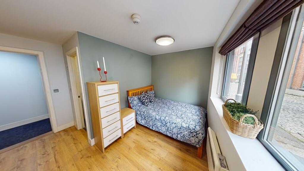 A cozy single bedroom featuring a wooden floor,...