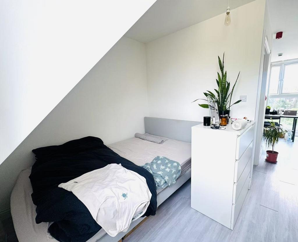 A well-lit bedroom featuring a simple bed with ...