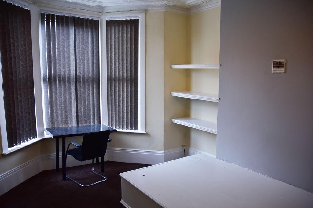 A modest bedroom with a bay window covered with...
