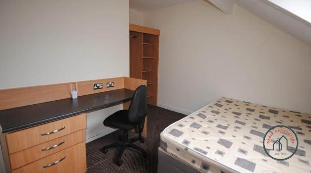 A tidy single bedroom featuring a bed, study de...