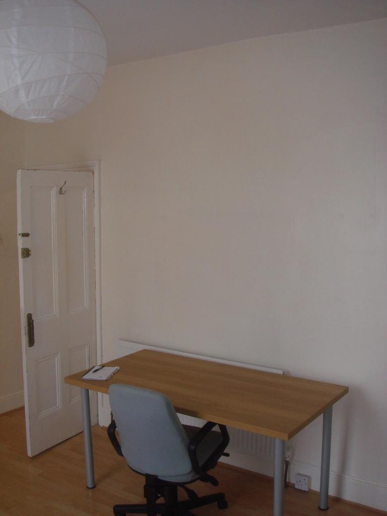 A simple, tidy bedroom with a wooden desk and a...