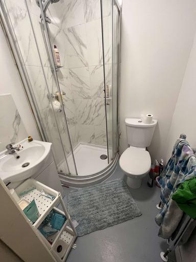 A modern compact bathroom featuring a corner sh...