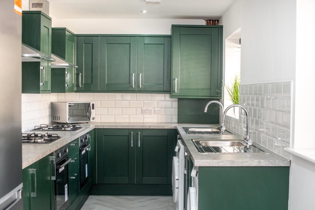 A modern kitchen featuring stylish green cabine...