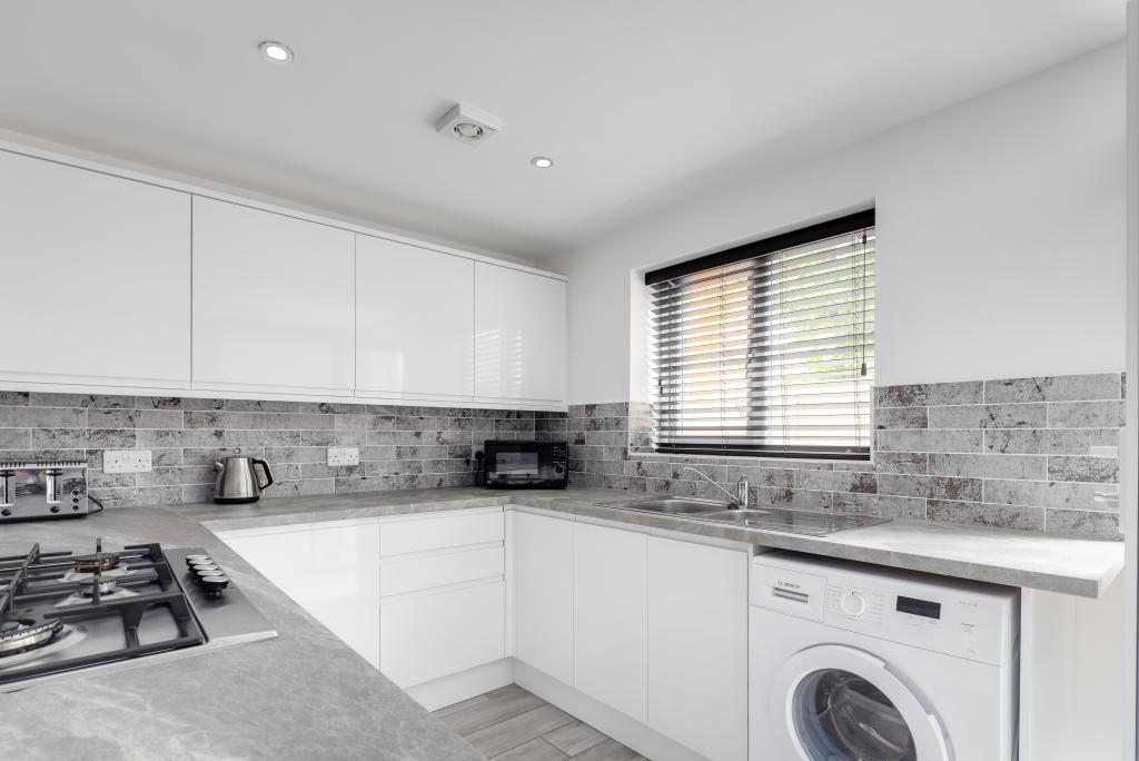 A modern, well-lit kitchen with white cabinets,...