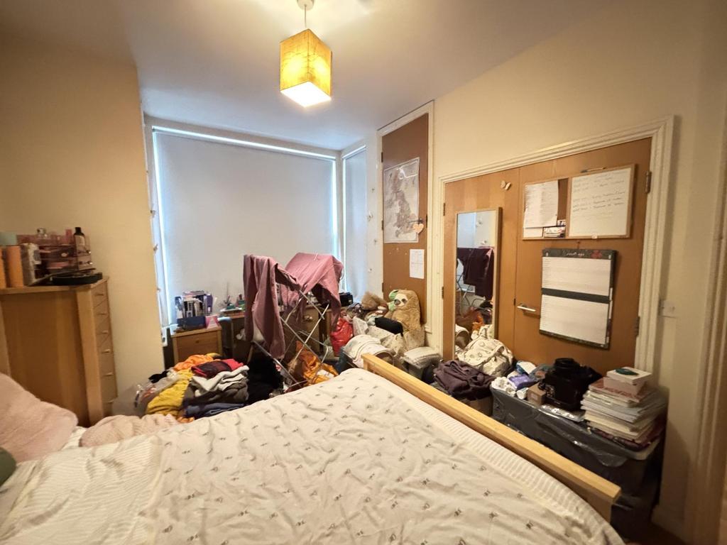 A cozy bedroom with a simple bed, cluttered sur...