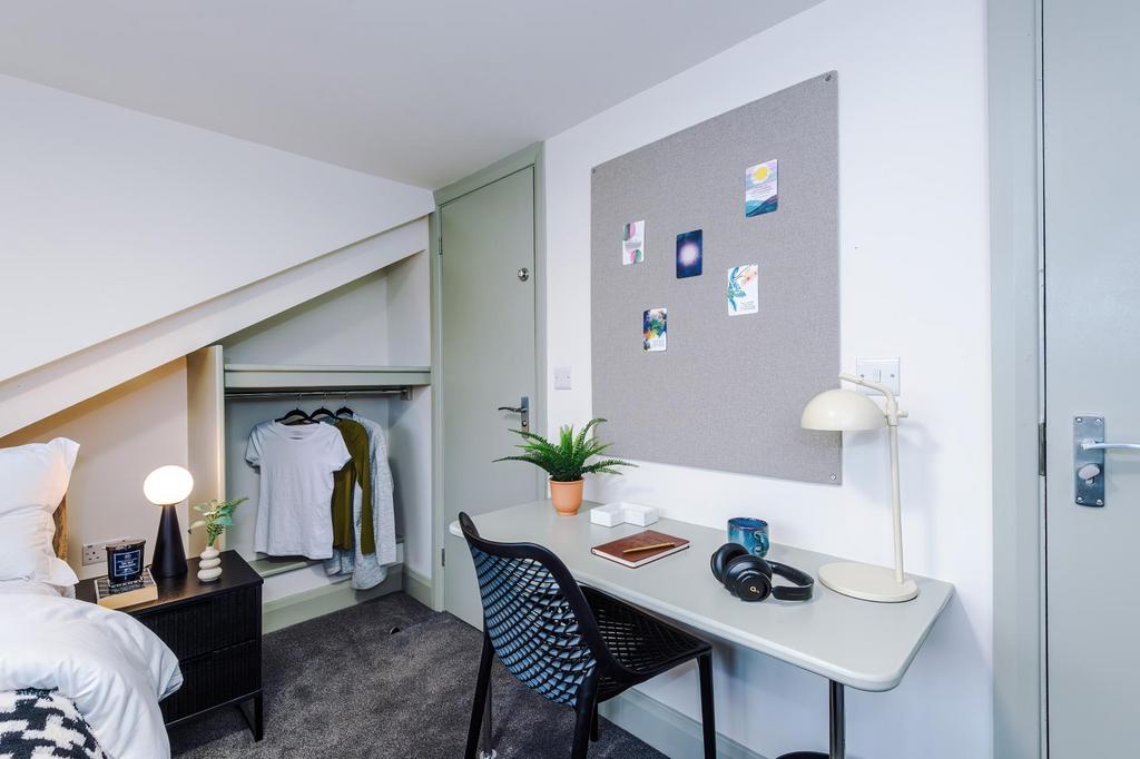 Bright, neatly arranged single bedroom with a c...