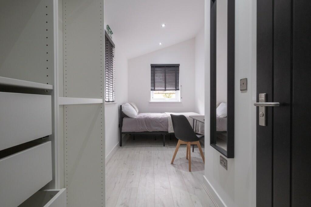 A clean and modern single bedroom with white wa...