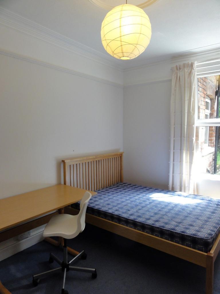 A clean, well-lit room featuring a single bed w...