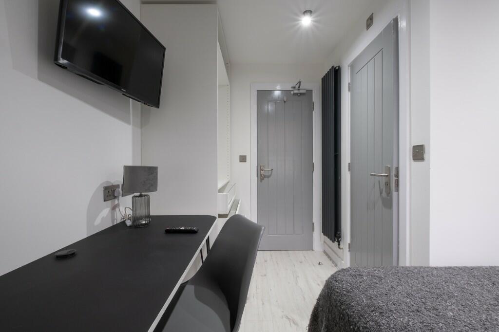 Bright, modern single bedroom with a mounted TV...