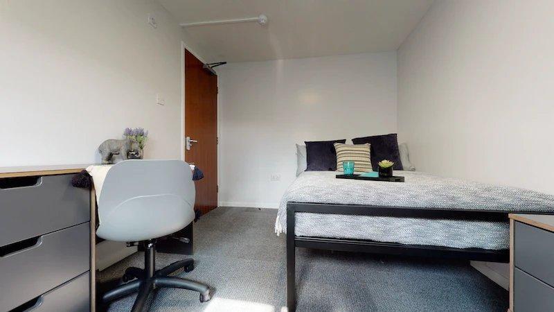 A tidy student bedroom featuring a bed, study d...