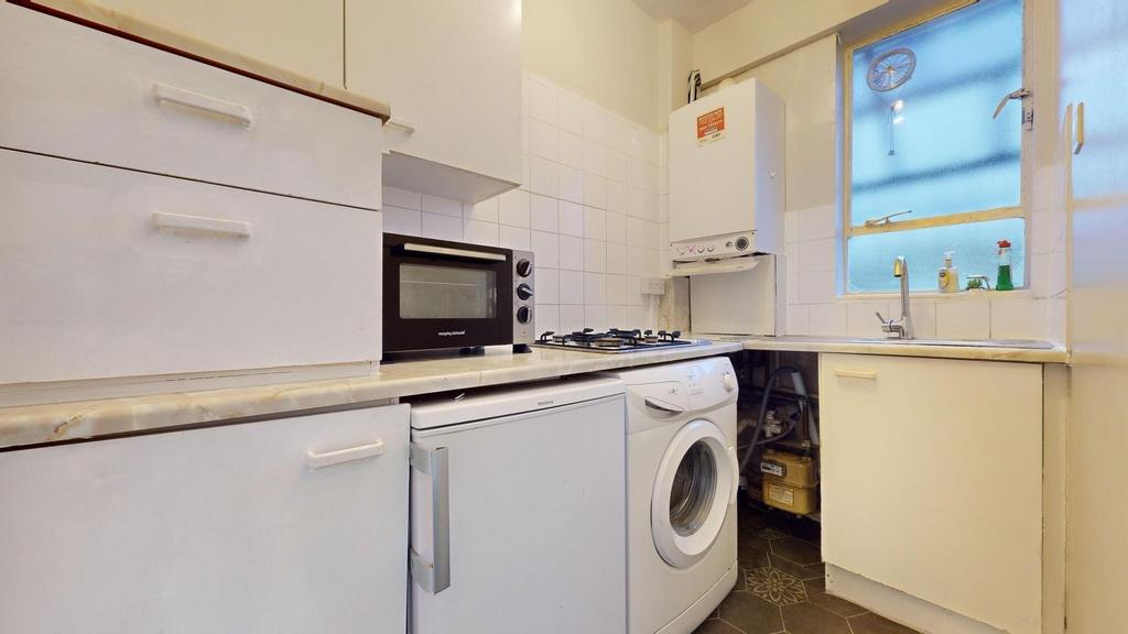 A compact kitchen featuring white cabinetry, a ...