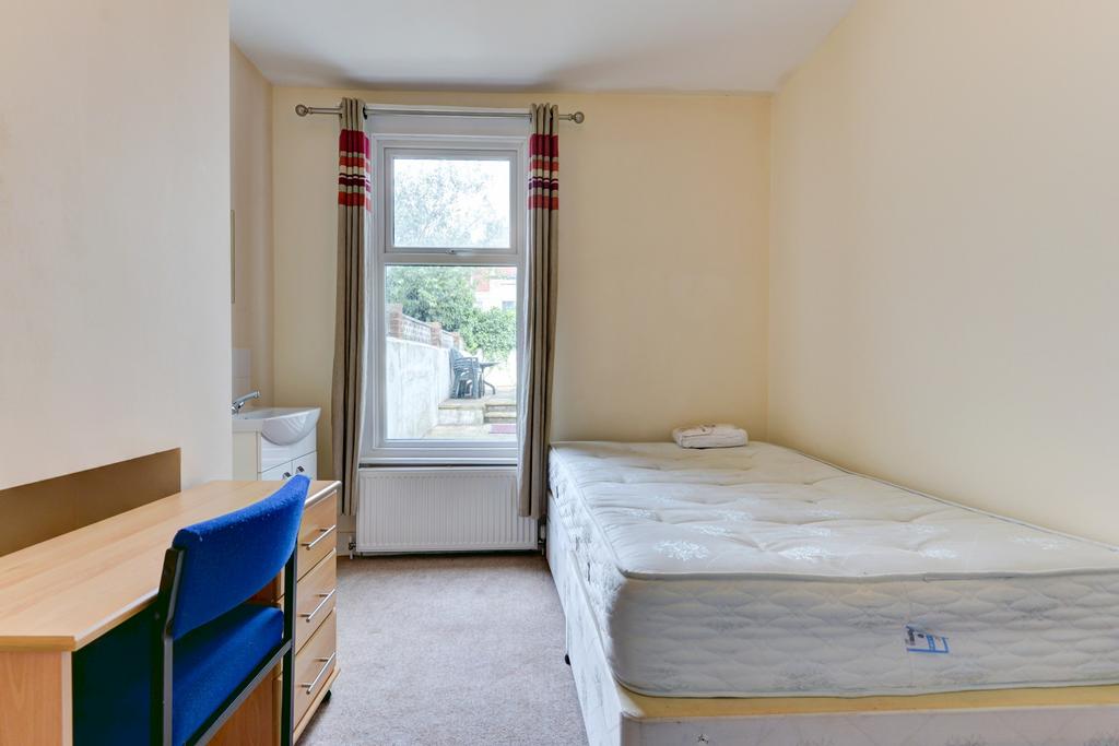 A bright, cozy single bedroom featuring a comfo...