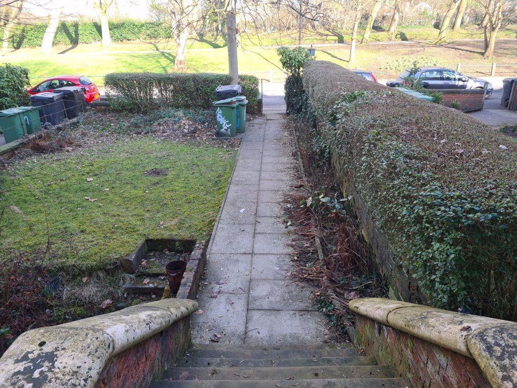 Paved front pathway flanked by well-kept hedges...