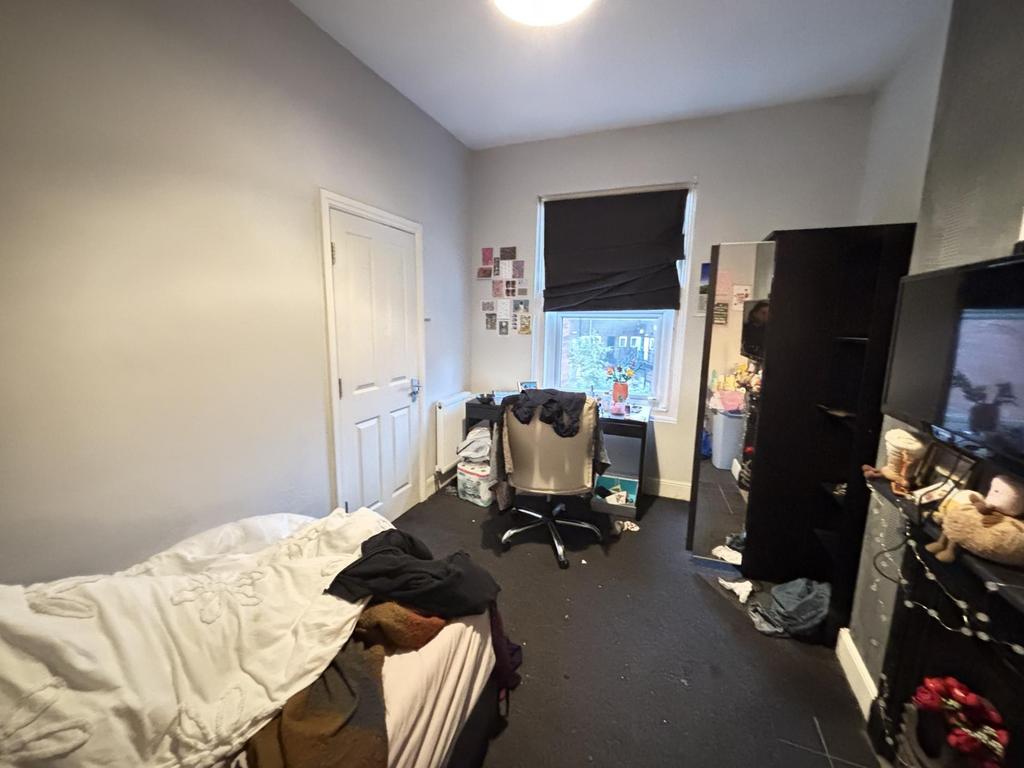 A cozy bedroom with a simple bed, window with a...