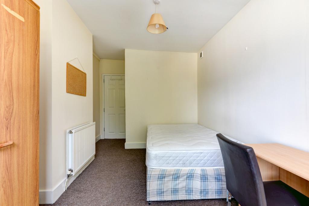 A cozy single bedroom featuring a bed, a small ...