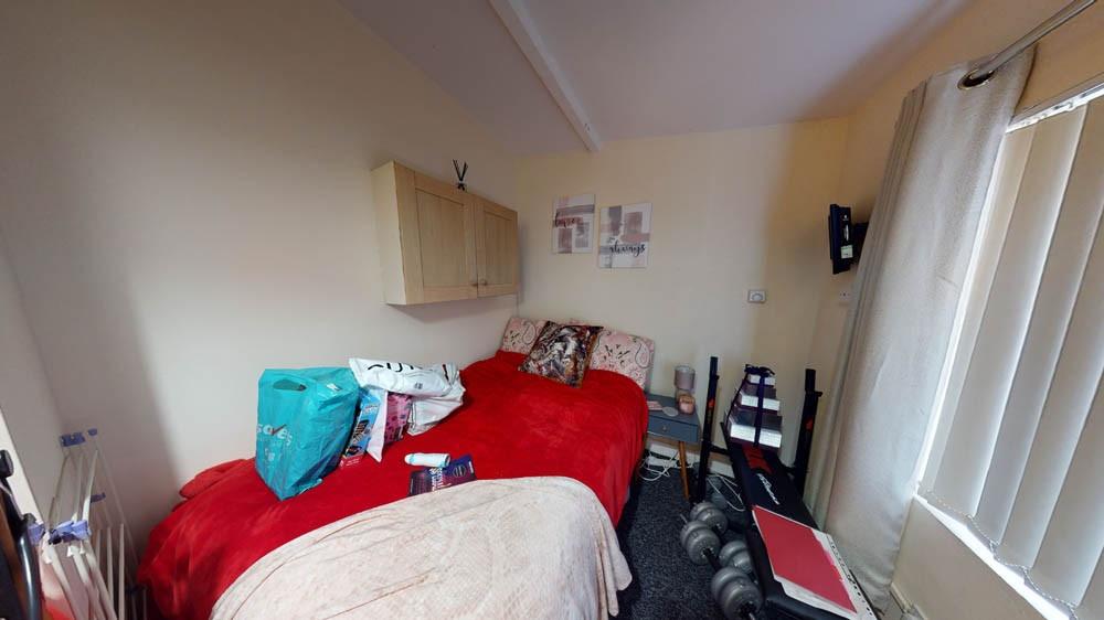 A cozy single bedroom featuring a red bedspread...