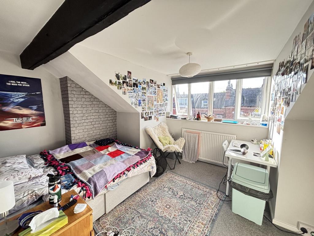 A cozy bedroom featuring a single bed, a desk, ...