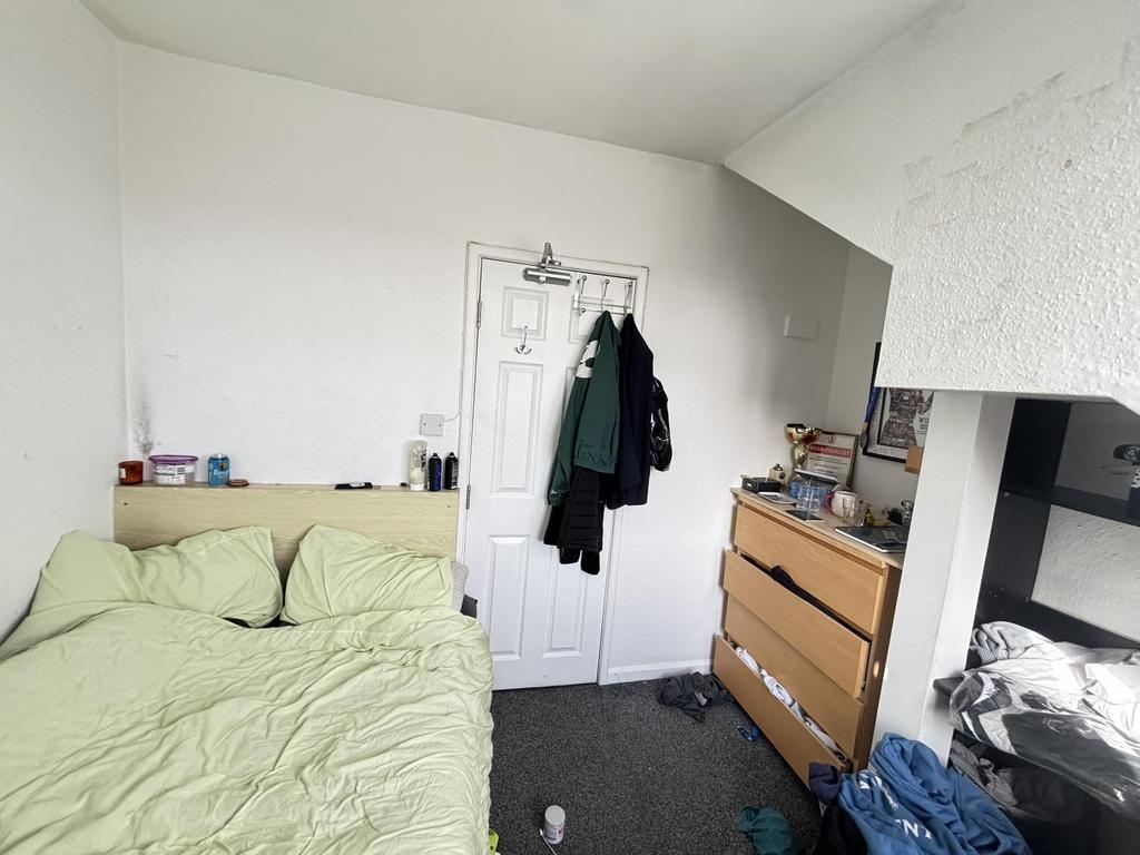 A modest bedroom with a bed, some clothing, and...