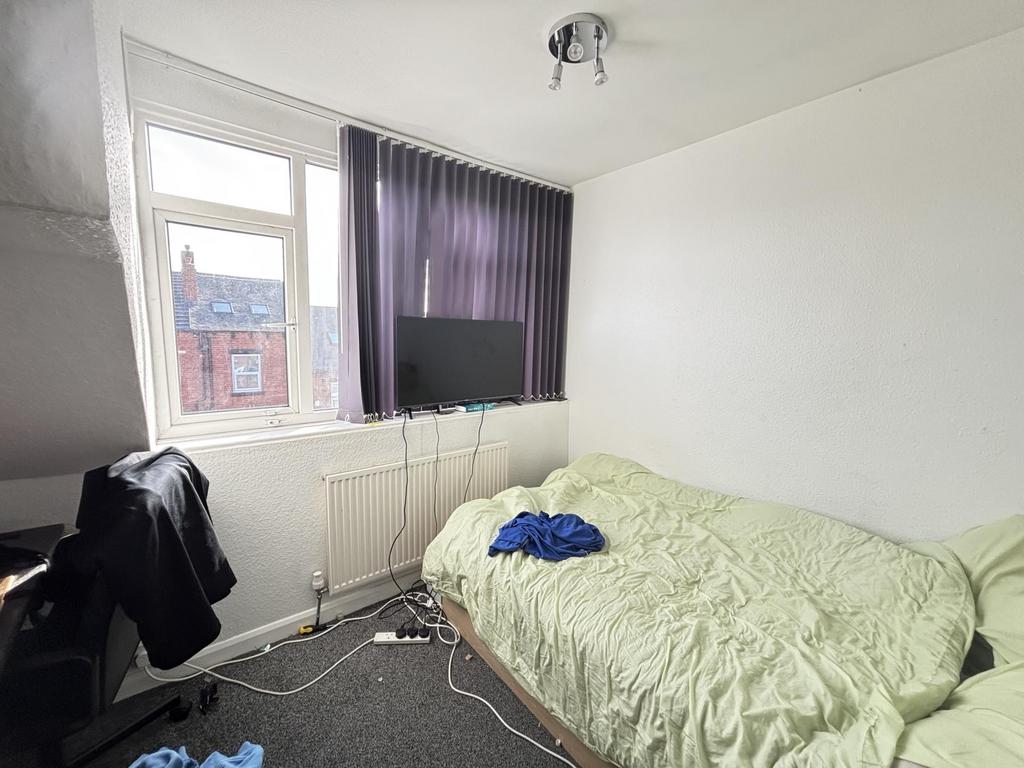 A modest bedroom featuring a single bed, a wind...