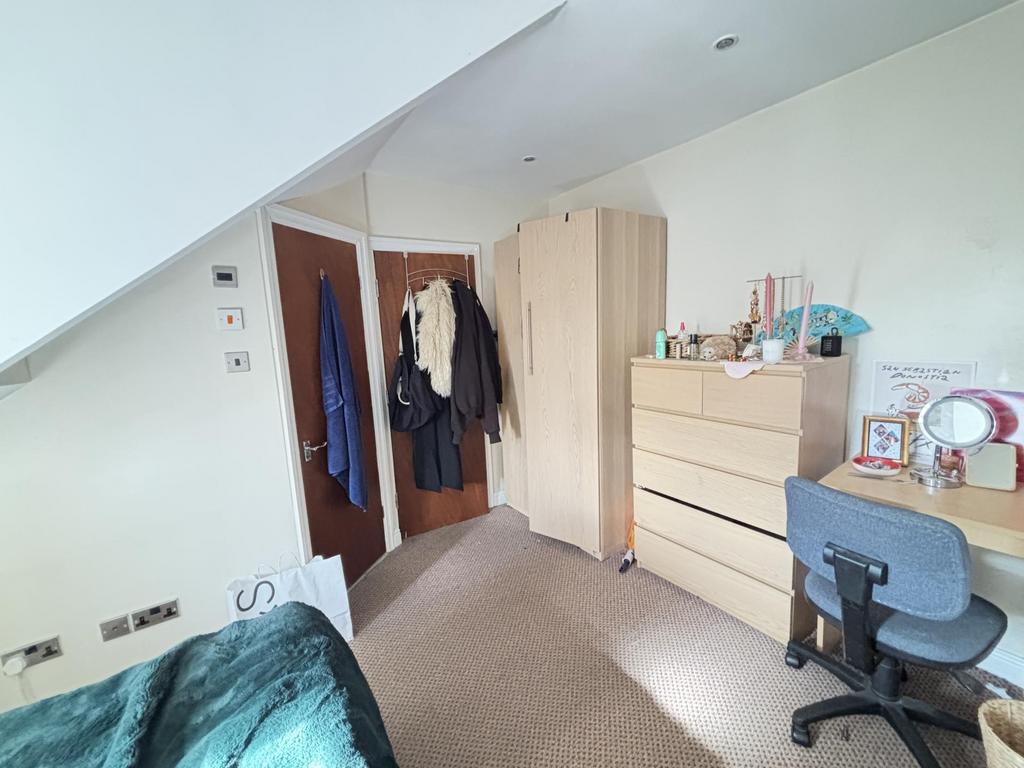 A well-lit bedroom featuring a bed, a desk with...