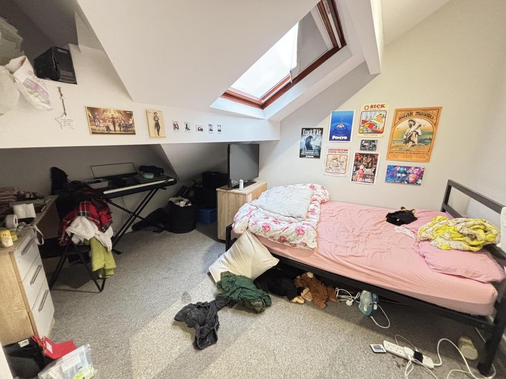 A cluttered bedroom with unmade bed and persona...