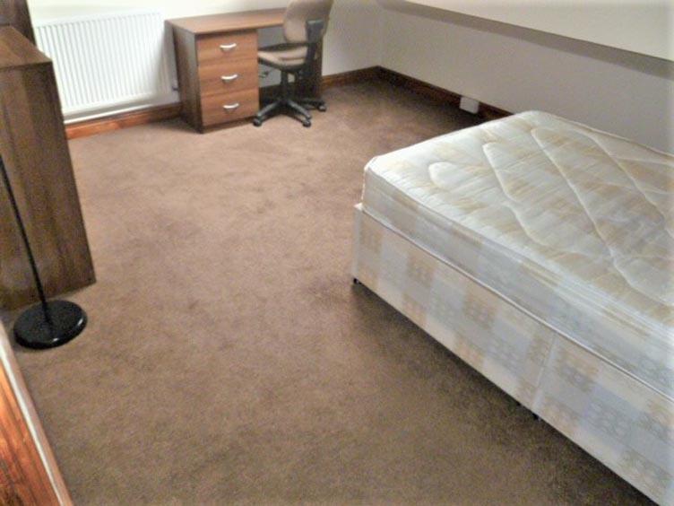 A modest bedroom featuring a single bed, a smal...