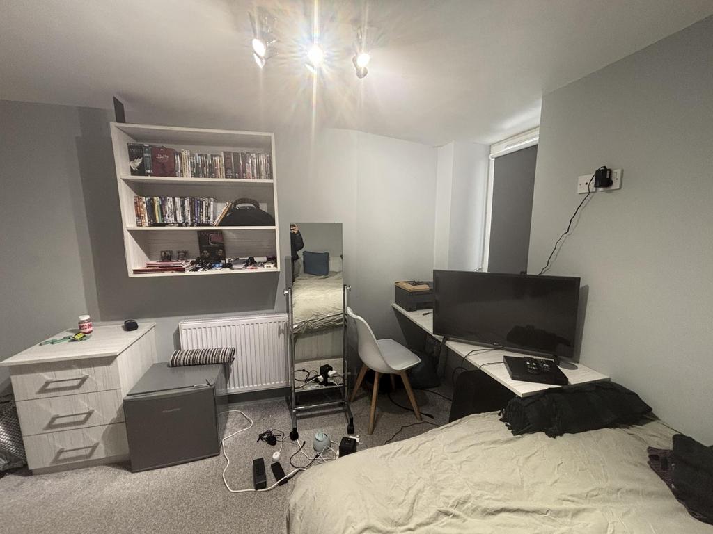 A well-lit bedroom featuring a large bed, a des...