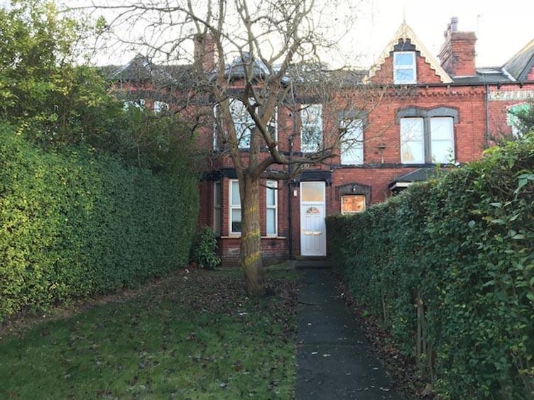 Red-brick terraced house set back behind a hedg...