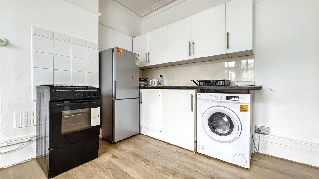 Bright compact kitchen with white cabinetry, in...