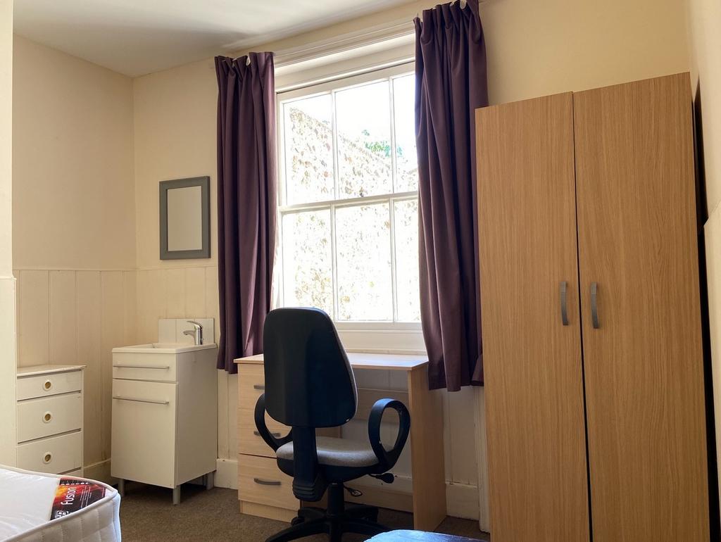A bright single bedroom featuring a window with...