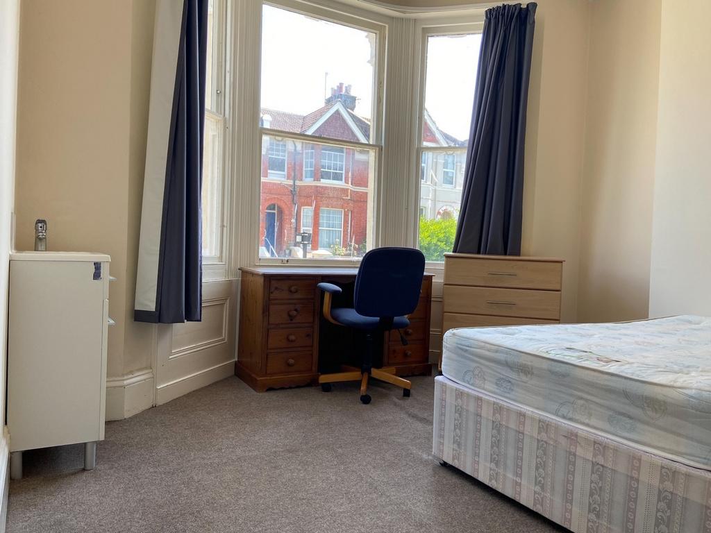 A bright and tidy bedroom featuring a large win...