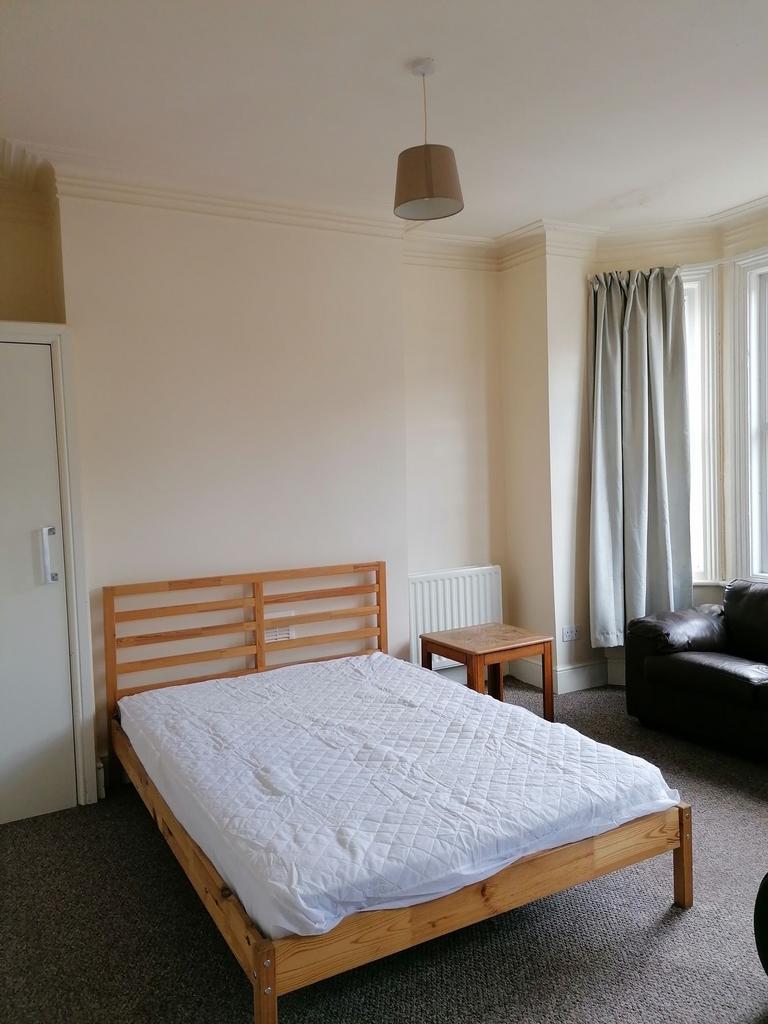 Bright double bedroom with a simple wooden bed ...