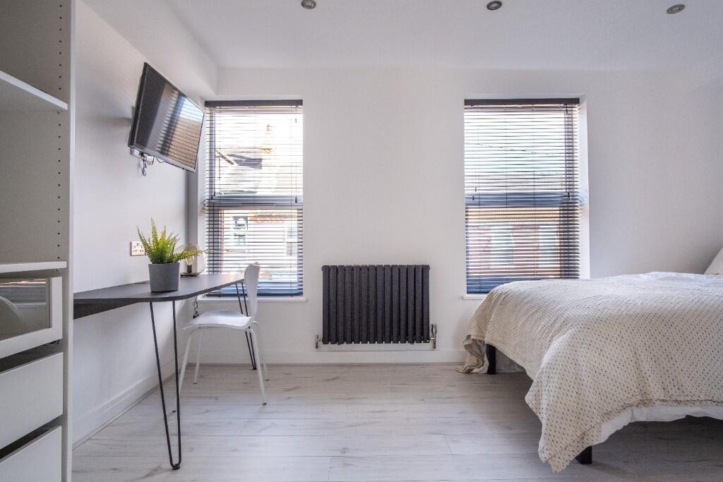 A bright, tidy bedroom with two large windows, ...