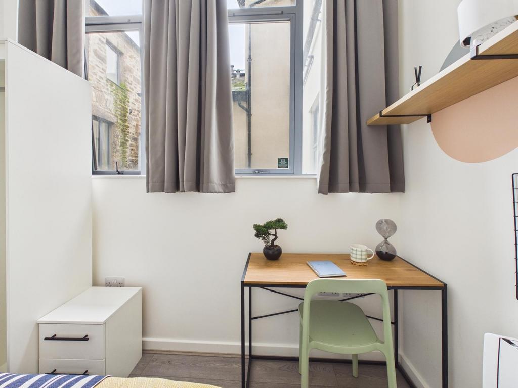 Bright, neat single bedroom with a desk by a la...