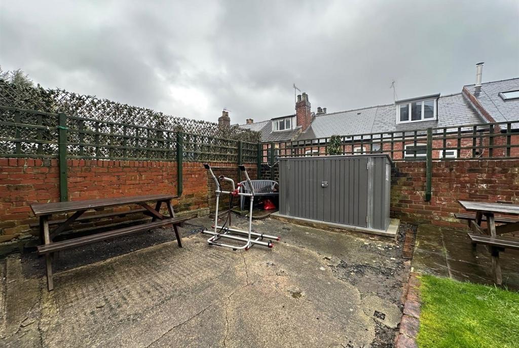 Enclosed paved garden area with brick walls, be...
