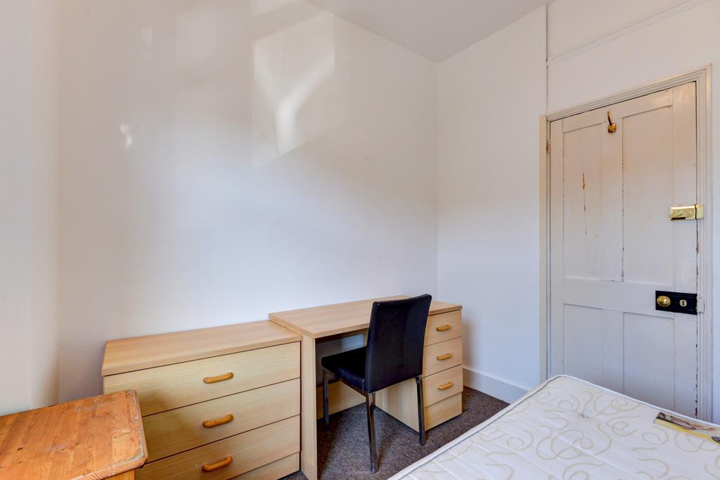 A cozy single bedroom featuring a simple desk a...