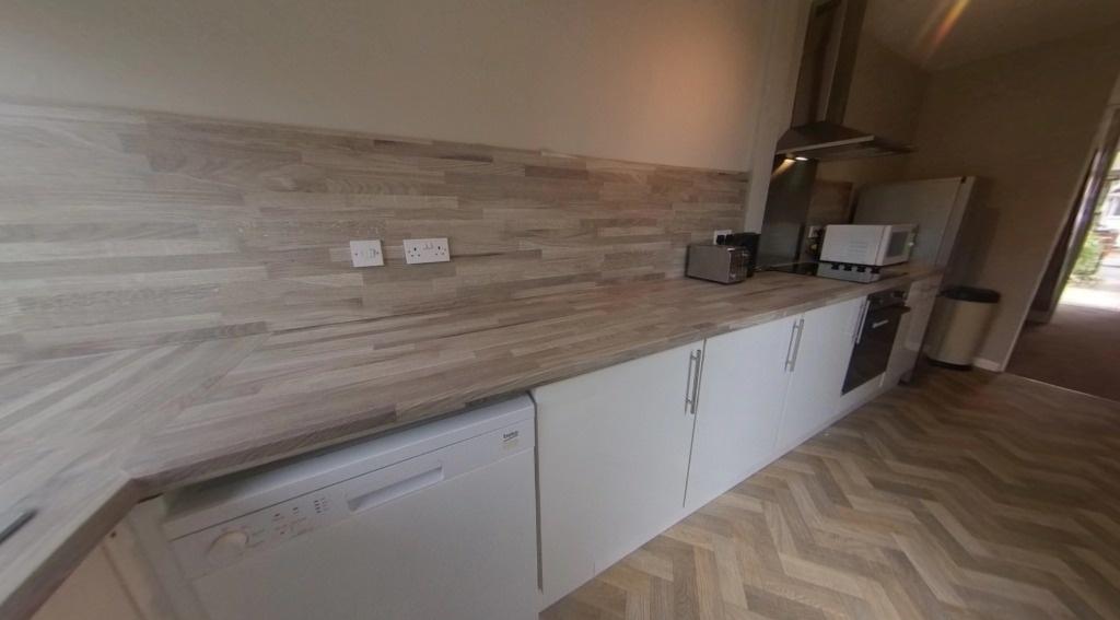 Long modern kitchen with wood-effect worktops a...